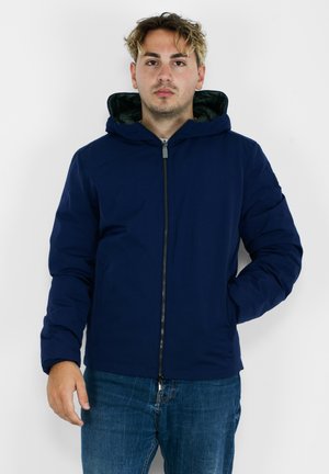 Giacca con zip di colore blu navy, dotata di cappuccio, con un esterno liscio, design imbottito e rivestimento interno verde a contrasto.