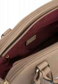 Interno di una borsa beige con una fodera bordeaux, dotata di un vano con cerniera, materiale texturizzato e finiture in hardware dorato.