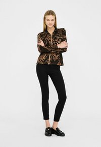 Giacca con stampa leopardata, con chiusura a zip, in tessuto marrone e nero, abbinata a pantaloni neri aderenti e mocassini neri. Design e texture semplici.