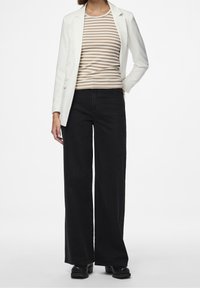 Valkoinen bleiseri beige- ja ruskearaitaisen ribbineulepuseron päällä, yhdistetty mustiin leveälahkeisiin farkkuihin. Sujuva pinta, siistit linjat ja vähäiset metalliosat.