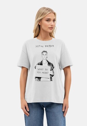 White cotton t-shirt featuring a black-and-white graphic of a person holding a sign that reads "WHAT DO YOU MEAN?" with block lettering.