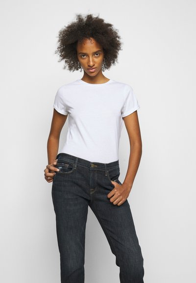 T-shirt bianca in cotone con maniche arrotolate, abbinata a jeans in denim blu scuro con chiusura a bottone e tasche laterali.
