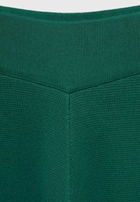 Detailný pohľad na zelenú rebrovanú pleteninu s chevronovými švovými detailmi pozdĺž stredu a horných okrajov.