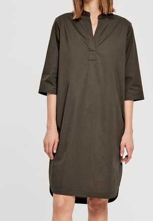 Locker sitzendes olivgrünes Kleid mit Dreiviertelärmeln, Stehkragen und V-förmigem Ausschnitt, getragen von einer Person, die am Hals und an den Knien beschnitten ist.