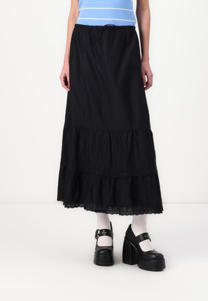 Gonna maxi nera a strati con design arricciato, bordo in pizzo ad occhielli all'orlo e vita elasticizzata. Modello che indossa scarpe platform nere e calzini bianchi.
