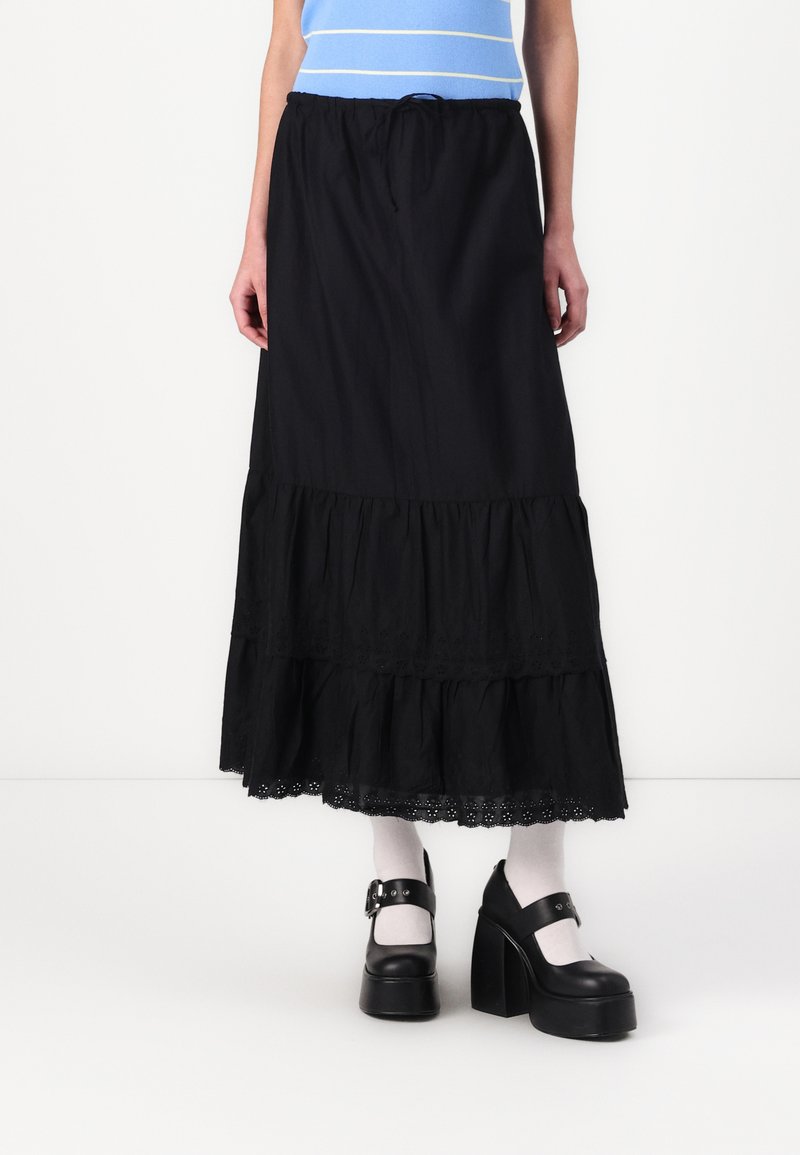 Gonna maxi nera a strati con design arricciato, bordo in pizzo ad occhielli all'orlo e vita elasticizzata. Modello che indossa scarpe platform nere e calzini bianchi.