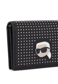 Portafoglio in pelle nera con borchie argentate, design pieghevole e un emblema di un personaggio con capelli bianchi e occhiali da sole sulla parte anteriore.