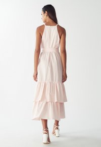 Vestido en capas de color rosa claro con rayas verticales blancas, que presenta un corsé ajustado, tirantes spaghetti ajustables y un dobladillo con volantes.