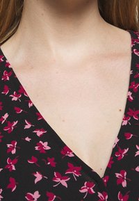 Zwarte kleding met een bloemenpatroon in tinten van roze. Heeft een V-halsontwerp en een zachte, gladde stoftextuur.