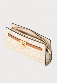 Beige canvas portemonnee met een MK-monogram patroon, bruin leren accent, gouden hardware, ritssluiting en een platte rechthoekige vorm.