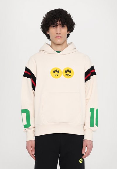 Cream hoodie with front pocket, featuring yellow graphic with black paw prints and teeth. Black stripes with red and green accents on sleeves.