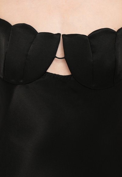 Zwarte satijnen top met een decoratieve scalloped halslijn. Heeft een open rug met een dunne elastische band voor een goede pasvorm. Glad materiaal over de hele top.