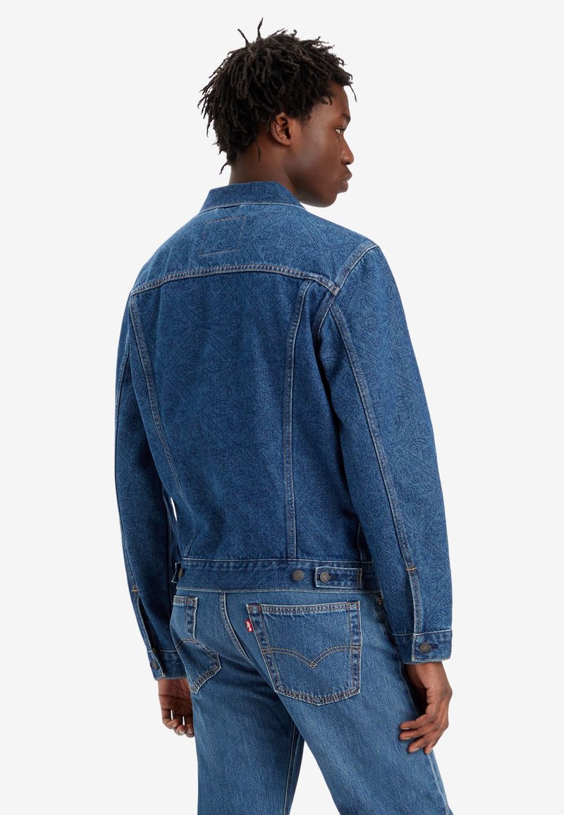 Veste en denim en tissu bleu à motifs avec un col, fermeture à deux boutons et détails au niveau du dos. Comprend des poches classiques et des coutures.