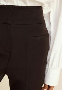 Pantalons noirs ajustés en tissu lisse, dotés d'une taille haute et d'une poche arrière discrète. Le design présente des lignes épurées et une silhouette ajustée.