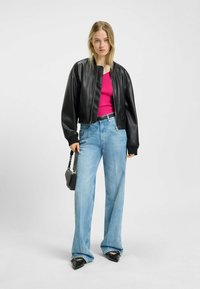 Svart croppad läderbomberjacka över en rosa ribbad topp, i kombination med vida ljusblå denimjeans och svarta spetsiga skor.