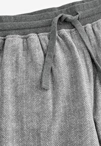 Grau gemusterte Lounge-Hose im Fischgrätenmuster mit elastischem Bund und gebundenem Kordelzug für eine verstellbare Passform.