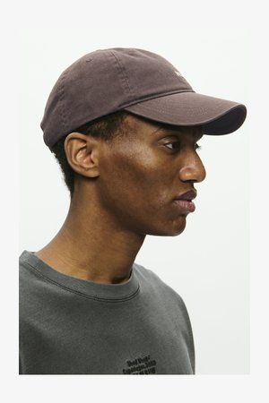 Gorra de béisbol de algodón en púrpura oscuro con visera curvada. Textura suave, con bordados mínimos, llevada con un sudadera gris.