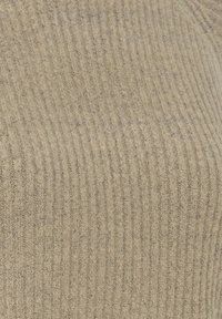 Gros plan sur un tissu beige en maille côtelée avec une texture douce et duveteuse et des rainures verticales espacées de manière uniforme.