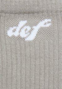 Grå strikkede sokker med ribbet struktur og et hvidt logodesign. Materialet ser blødt og strækbart ud med et ensartet mønster.