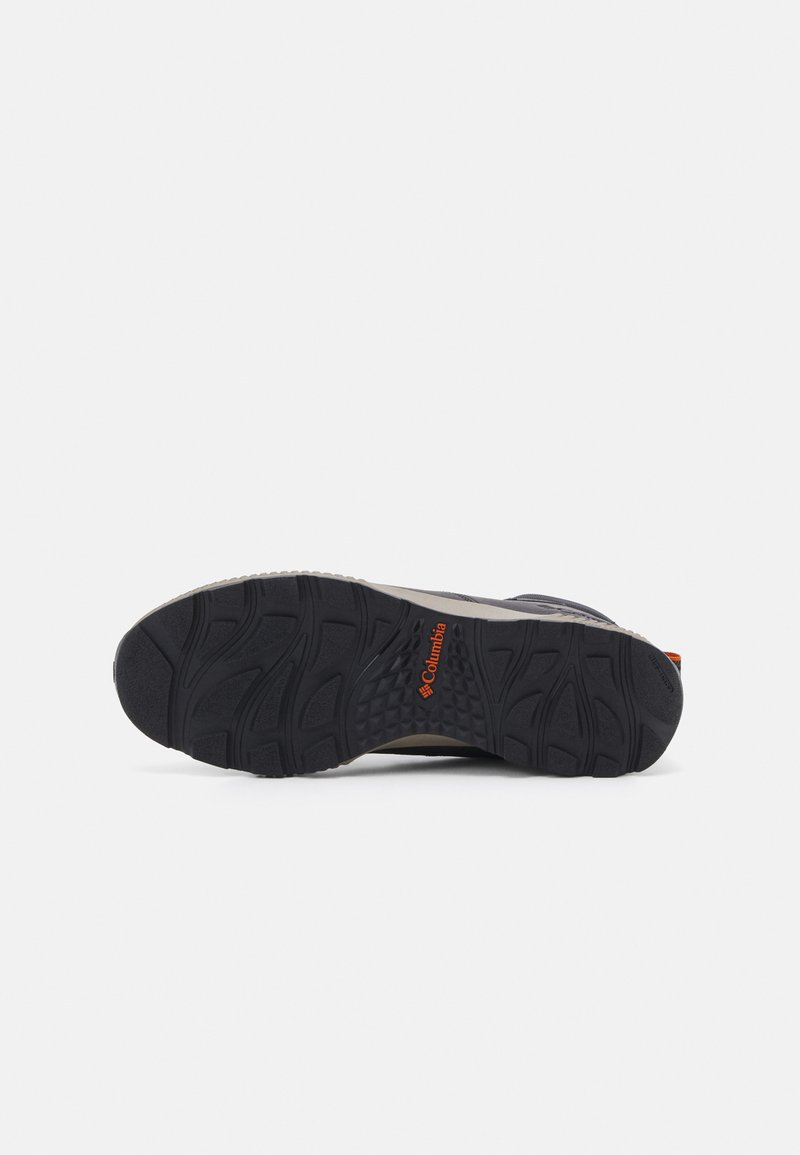 Suela de zapato de senderismo negra con agarre texturizado, logo de Columbia en naranja, diseño robusto y una entresuela de color claro en contraste.