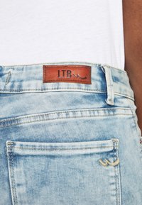 Vaqueros de mezclilla azul claro con una etiqueta de cuero marrón de LTB. Entre sus características se encuentran los bolsillos traseros y un efecto de lavado desgastado con detalles de costura.