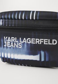 Juodas audinio maišelio su užtrauktuku, dekoruotas mėlynu ir baltu grafiniu piešiniu, su įspaustu „KARL LAGERFELD JEANS“ logotipu.