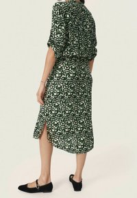 Vestido verde con estampado, de manga corta, corte holgado, longitud midi, con una abertura lateral y cintura elástica, combinado con zapatos planos negros.