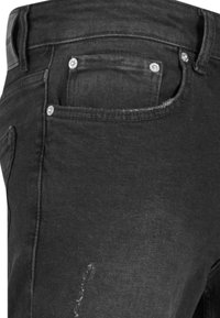 Gros plan d'un jean denim noir montrant une poche avant avec des rivets en métal et une zone décolorée et usée sur la cuisse.
