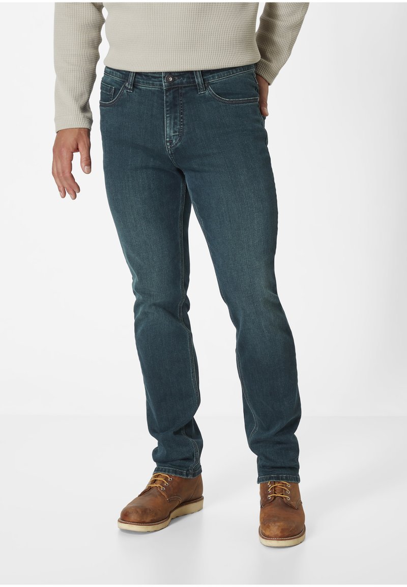 Dark blue denim jeans with a slim fit, featuring five pockets, contrasting stitching, and a textured, ribbed beige sweater.