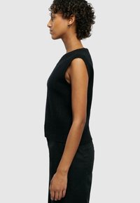 Zwarte mouwloze gebreide top met een ronde halslijn, aansluitend silhouet en geribde zoom, weergegeven op een model van opzij.