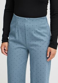 Lichtblauwe broeken met een zachte textuur, voorzien van donkerblauwe stippen, een hoge taille en plooien, gecombineerd met een zwart langemouwen top.