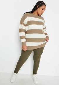 Brun och vit randig oversized tröja med ribbat mönster, i kombination med olivgröna slim-fit cargo-byxor med sidofickor. Vita sneakers.