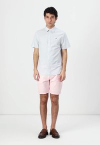 Lys blå kortermet skjorte med knapper, rosa shorts og brune slip-on sko. Glatt stoff med subtile detaljer og en behagelig passform.