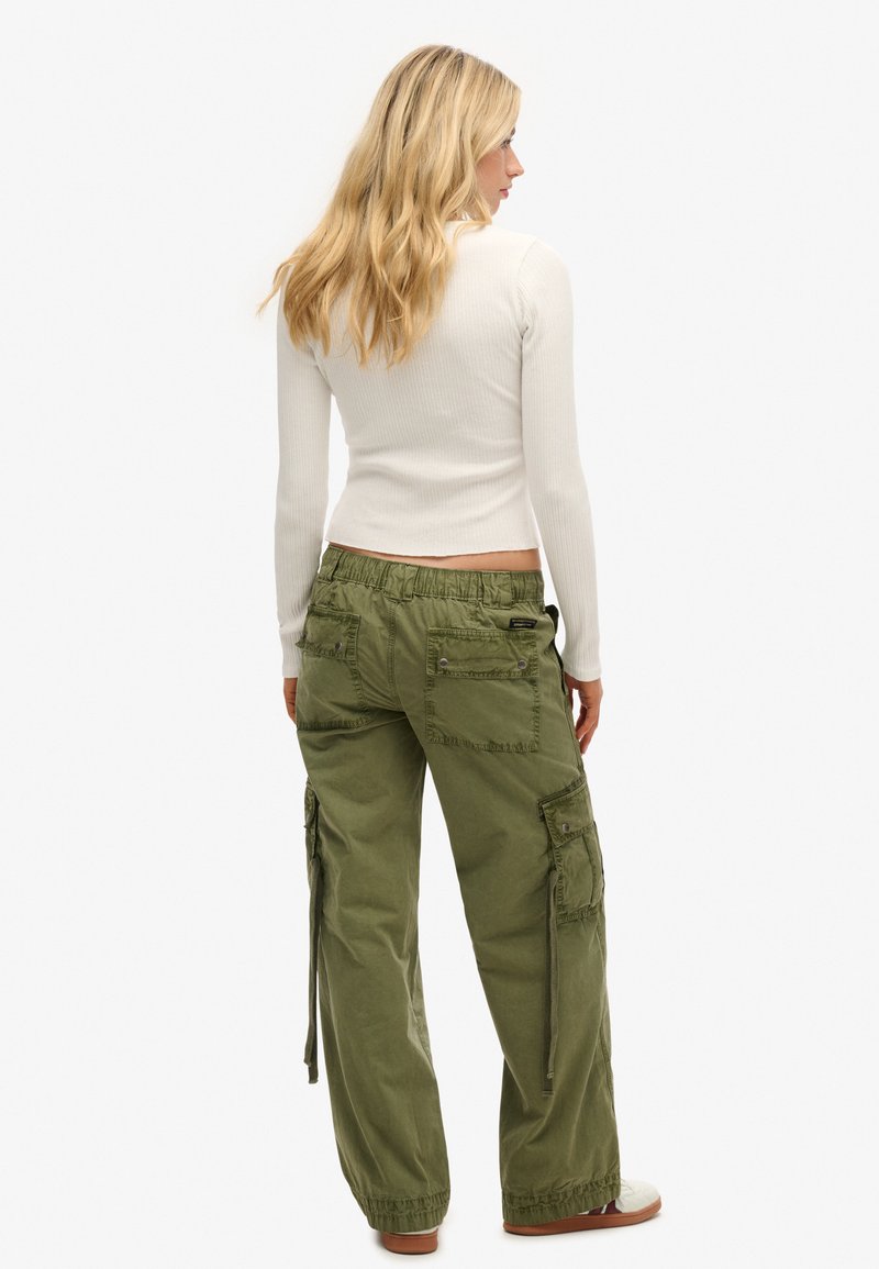 Losse, olijfgroene cargobroek met meerdere zakken, elastische tailleband en trekkoorddetails. Gecombineerd met een aansluitend wit longsleeve shirt.