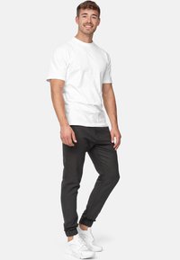 Camiseta de algodón blanca combinada con joggers oscuros de corte ajustado y zapatillas blancas. Los joggers tienen tobillos con puños y bolsillos laterales.