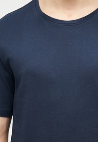 Primo piano di una persona che indossa una T-shirt semplice blu navy con scollo rotondo, maniche corte e tessuto dalla trama liscia.