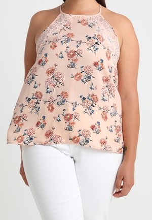 Haut sans manches pêche à col licou avec bordure en dentelle et imprimé floral, porté avec un pantalon blanc, présenté sur une personne de la nuque aux hanches.