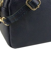 Zwarte leren handtas met een gestructureerd oppervlak, gouden accenten en blauwe stikdetails. Rechthoekige vorm met een afneembare band.