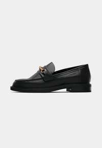Schwarze Lederloafer mit niedrigem Absatz, versehen mit einer goldfarbenen Kettenakzentierung über dem Rist und kontrastierenden Nähten entlang der Kante.