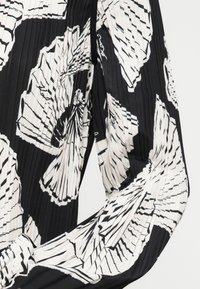 Melnā un baltā krāsā pleatota auduma ar tauriņu rakstu, kas izceļ gludu tekstūru un plūstošu drapējumu. Izceļas ar garām piedurknēm un noapaļotu kakla izgriezumu.