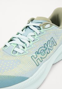 Chaussure de course HOKA avec une tige en mesh bleu clair et vert menthe, des détails texturés, des lacets plats et une épaisse semelle blanche.