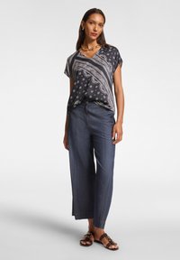 Top a righe in bianco e nero con scollo a V e maniche corte; abbinato a pantaloni wide-leg in denim scuro e sandali marroni con fibbia dorata.