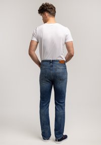 Niebieskie dżinsy o klasycznym, prostym kroju nogawek, z naszywką ze skóry z tyłu oraz dwiema tylnymi kieszeniami. Noszone z białym T-shirtem.