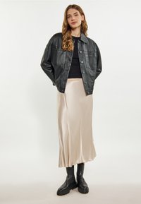 Jachetă oversized din piele neagră, fustă midi din satin bej și botine cu talpă groasă negre. Texturi netede și materiale contrastante.