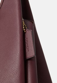 Burgundy leather handbag with textured finish, featuring a gold chain detail and a tag embossed with "COACH."