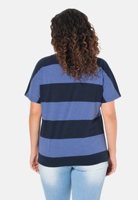 Camiseta a rayas azul y marino con un corte holgado, mangas cortas y una textura suave, vista desde atrás. Jeans de color azul claro complementan el conjunto.