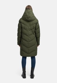 Puffet grøn jakke med stor hætte, prydet med diagonale quiltede mønstre, lange ærmer og knælang silhuet. Matchet med mørke jeans og støvler.