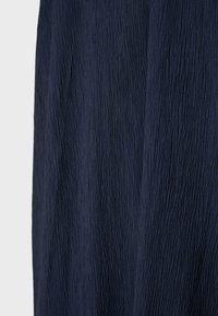 Tissu bleu marine foncé avec texture plissée verticale, montrant un gros plan détaillé du motif et des plis de la surface du matériau.