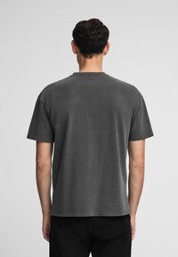 Camiseta de algodón gris con cuello redondo, mangas cortas y un corte relajado. Textura sutil. La vista posterior muestra un diseño simple sin adornos.