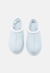 Gaiši zili čības ar mīkstu, pūkainu oderi, zamšādas virsmu, noapaļotu purngalu un baltu teksturētu apdari ap ieeju.